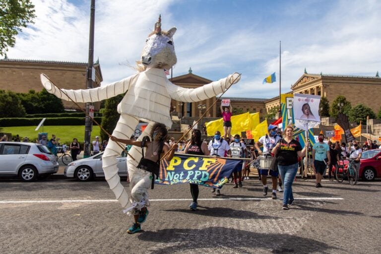 Samantha Rise leads a march demanding arts funding in a giant unicorn puppet