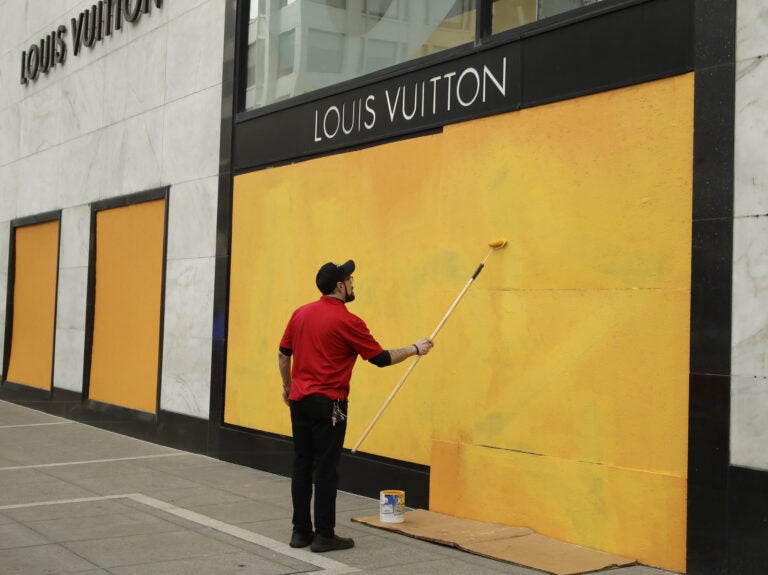 A worker paints over a Louis Vuitton storefront boarded up due to the coronavirus outbreak on March 30 in San Francisco.