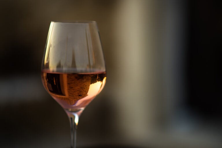 Picture in low key of glass of rose wine with reflection of old stone traditional provencal house in it. Rose wine in Provence, France. Light alcoholic drink.
