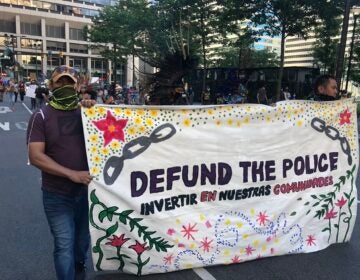 Activists at a rally in Center City hold up a sign demanding the mayor defund the PPD