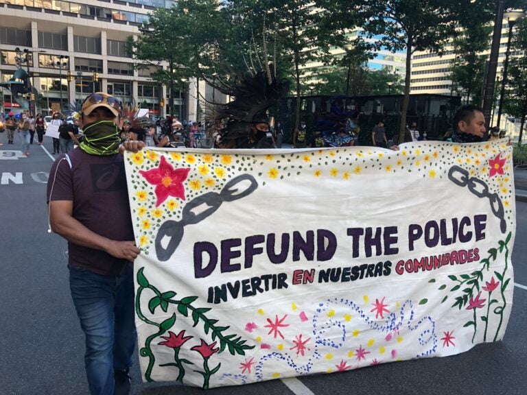 Activists at a rally in Center City hold up a sign demanding the mayor defund the PPD