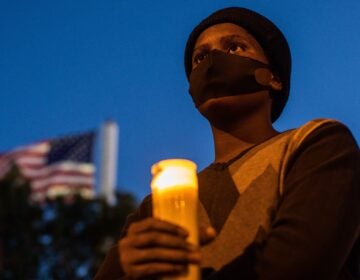 A man holds a candle during a vigil around a makeshift memorial at the tree where Robert Fuller was found dead hanging from a rope in Palmdale, Calif. Officials deemed Fuller's death a suicide, but his family wants an independent investigation.