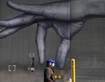 A man in a mask walks past a mural of a hand on the side of a building in N.Y.C in April.