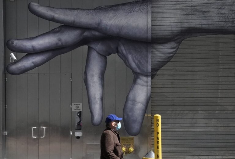 A man in a mask walks past a mural of a hand on the side of a building in N.Y.C in April.