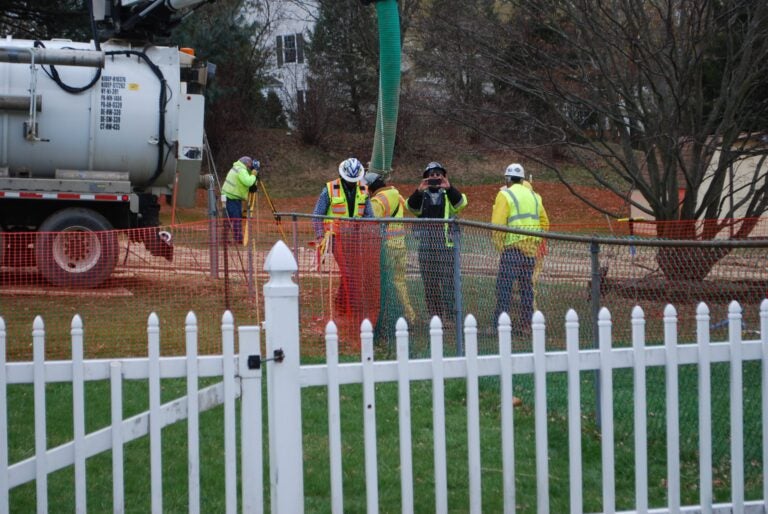 In this May 2018 photo, workers and contractors for Sunoco Pipeline investigate sink holes behind homes at Lisa Drive, West Whiteland Township, Chester County where the company has been drilling for construction of the Mariner East 2 and 2X pipelines. In the photo, a security guard is taking a picture of the reporter. (Jon Hurdle / StateImpact PA)