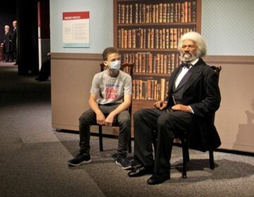 Caleb Cattell takes a seat beside a wax figure of Frederick Douglass at the Franklin Institute. The 13-year-old from Riverton, N.J., and his family were among the first wave of visitors when the Institute reopened on Wednesday. (Emma Lee/WHYY)
