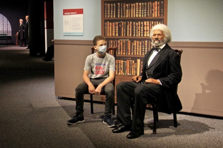 Caleb Cattell takes a seat beside a wax figure of Frederick Douglass at the Franklin Institute. The 13-year-old from Riverton, N.J., and his family were among the first wave of visitors when the Institute reopened on Wednesday. (Emma Lee/WHYY)