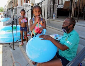 Taylor Corbin, 4, (center) helps block captain Roslyn Myers inflate a hopper ball