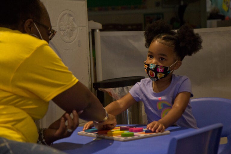 Kimrenee Patterson works on a puzzle, with Peyton, 2, at Patterson’s daycare in Philadelphia. (Kimberly Paynter/WHYY)