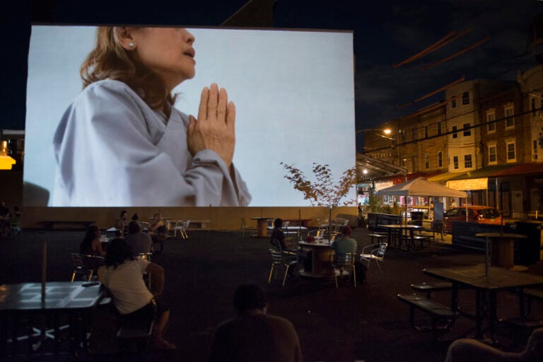 A woman holds her hands in a prayer position in the video by Kevin Nguyen projected during the 'Cleanse' exhibit in the Italian Market on July 11, 2020. (Photo by Lori Waselchuk)
