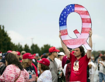 FILE - In this Aug. 2, 2018, file photo, David Reinert holding a Q sign waits in line with others to enter a campaign rally with President Donald Trump in Wilkes-Barre, Pa. A far-right conspiracy theory forged in a dark corner of the internet is creeping into the mainstream political arena. It's called QAnon, and it centers on the baseless belief that President Donald Trump is waging a secret campaign against enemies in the “deep state.”  (AP Photo/Matt Rourke, File)