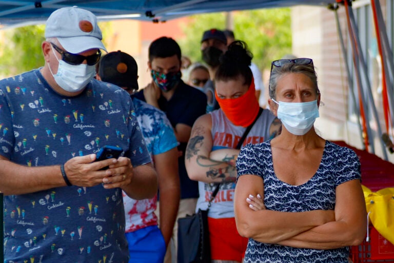 People waiting in line to enter a grocery store wear COVID-19 protective masks