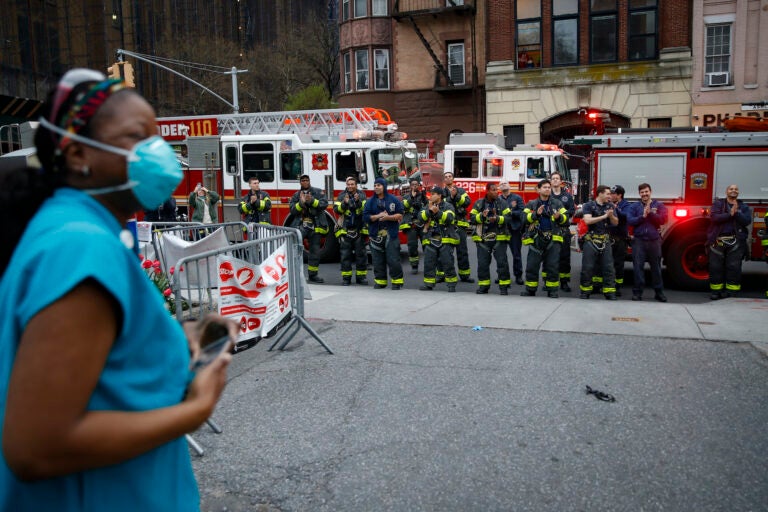 FDNY firefighters gather to applaud medical workers as attending physician Mollie Williams, left, wears personal protective equipment due to COVID-19 concerns outside Brooklyn Hospital Center, Tuesday, April 14, 2020, in New York. (AP Photo/John Minchillo)