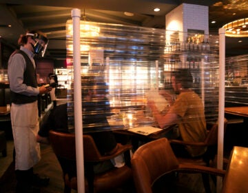 In this June 22, 2020, file photo, wearing a face shield, server Brandon Fricke, left, takes orders from dine-in customers surrounded by protective dividers at Water Grill seafood restaurant in Los Angeles. (AP Photo/Jae C. Hong)