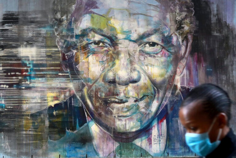 A masked woman walks past a mural of former President  Nelson Mandela in Cape Town, South Africa, Saturday July 18, 2020 as the country celebrates International Mandela Day. (AP Photo/Nardus Engelbrecht)
