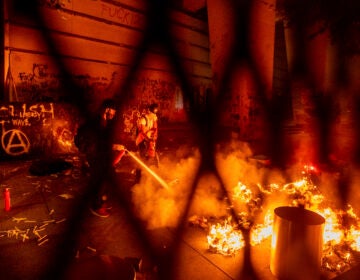 A protester extinguishes a fire set by fellow protesters at the Mark O. Hatfield United States Courthouse on Wednesday, July 22, 2020, in Portland, Ore. (AP Photo/Noah Berger)