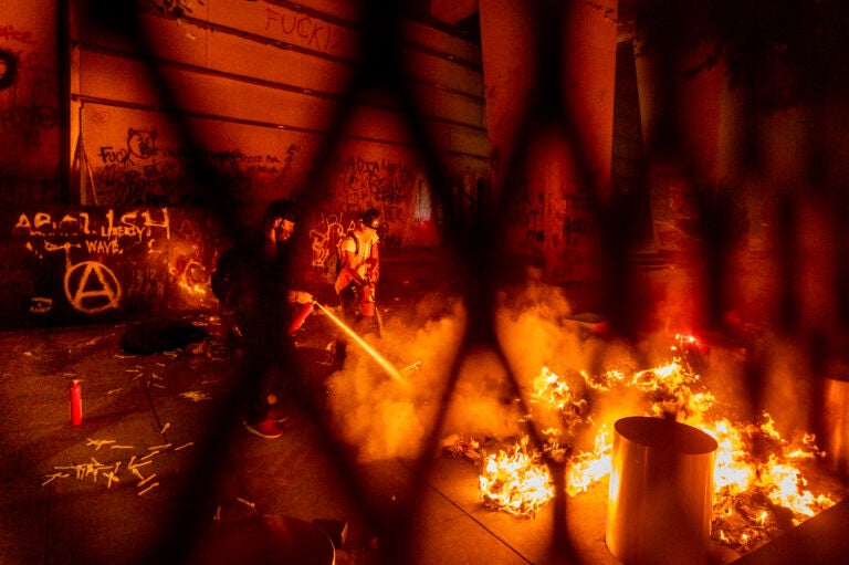 A protester extinguishes a fire set by fellow protesters at the Mark O. Hatfield United States Courthouse on Wednesday, July 22, 2020, in Portland, Ore. (AP Photo/Noah Berger)