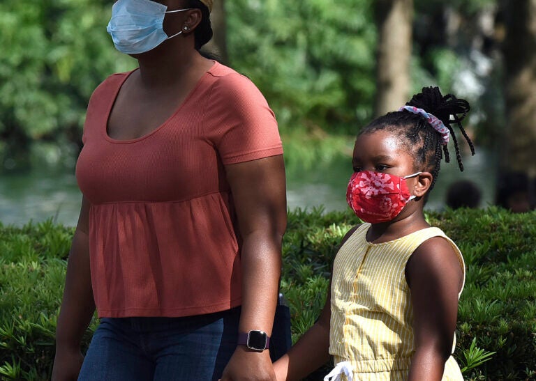 A child and her mother wear face masks while walking through a park