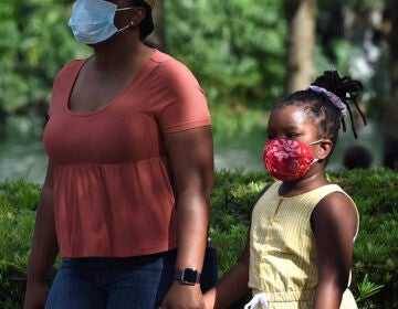 A child and her mother wearing face masks as a preventive measure walk at Lake Eola Park.