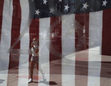 A passerby wears a mask out of concern for the coronavirus while walking past an American flag displayed in Boston on Tuesday. The U.S. has now recorded more than 3 million confirmed cases of the coronavirus.