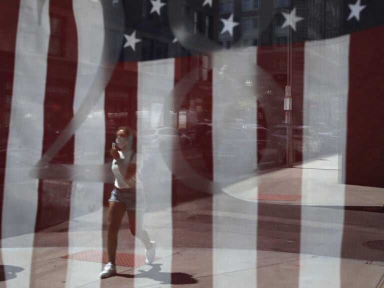 A passerby wears a mask out of concern for the coronavirus while walking past an American flag displayed in Boston on Tuesday. The U.S. has now recorded more than 3 million confirmed cases of the coronavirus.