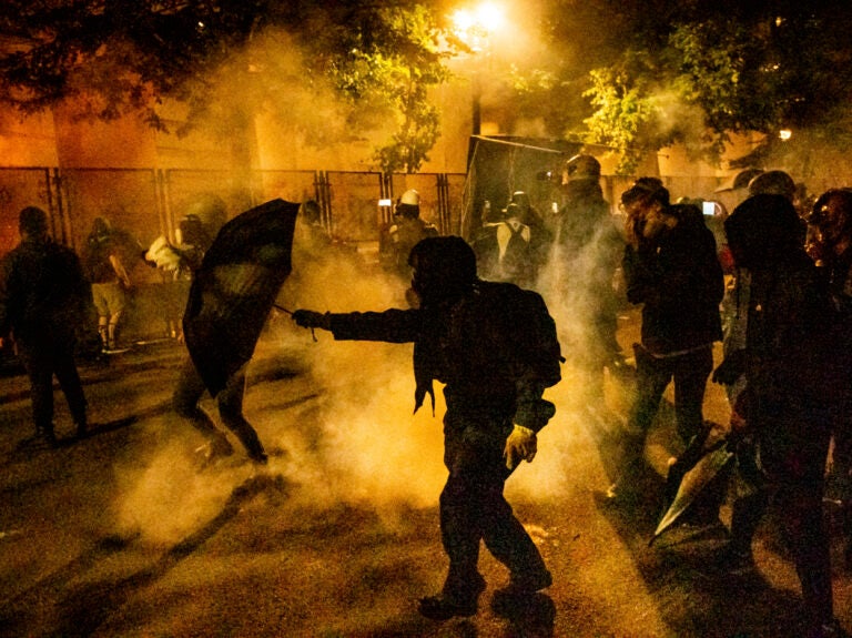 Protesters walk through chemical irritants deployed by federal agents in Portland, Ore. The inspector general of the Justice Department says he is investigating federal officers' roles in responding to protests in Portland and Washington, D.C. (Noah Berger/AP Photo)