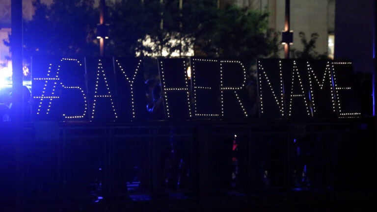 Protesters hold up a lighted sign reading 