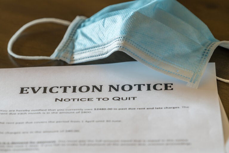 Defaulting renter with face mask receives letter giving notice of eviction from home on wooden table. (BackyardProductions/BigStock)