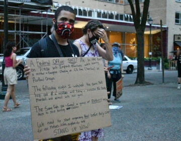 Jordan Johnson holds a sign detailing a recent incident with what he says were federal police in Portland, Oregon. (Brett Sholtis/WITF)