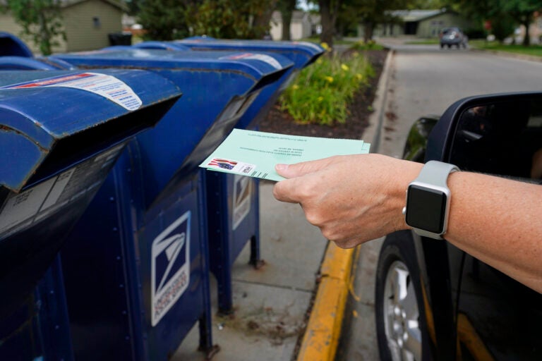 A person drops into a mail box applications for mail-in ballots