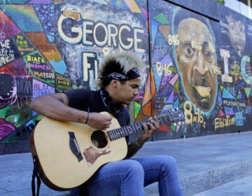 Shane Braswell, who has participated in Black Lives Matter protests this summer, plays guitar in front of a mural covering the entrance to an Apple store, Aug. 27, 2020 in Portland, Ore. Braswell said President Donald Trump's portrayal of Portland as a violent city overcome by mobs of protesters is inaccurate and grossly exaggerated. 