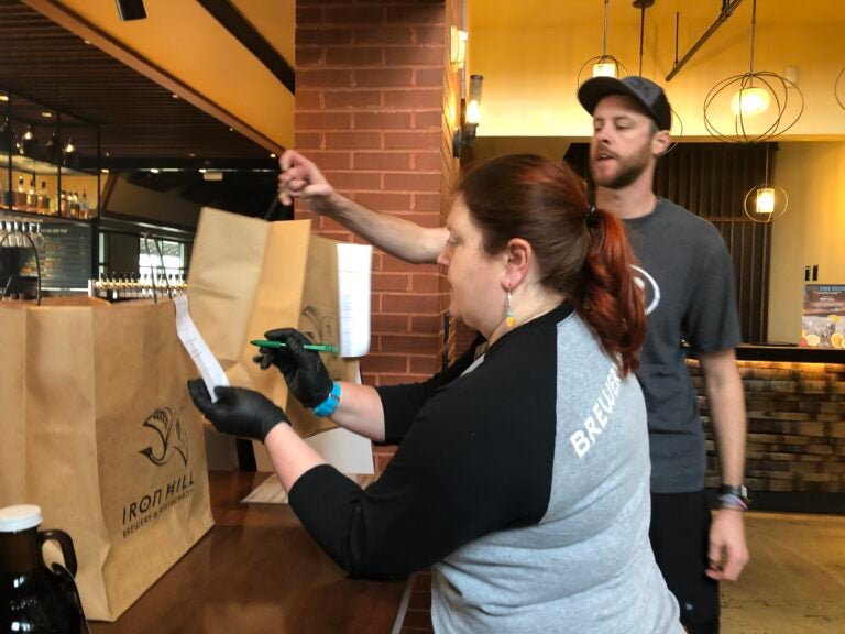 Moriah Guise and Dustin Mitchell check takeout orders at Iron Hill Brewery. (Cris Barrish/WHYY)