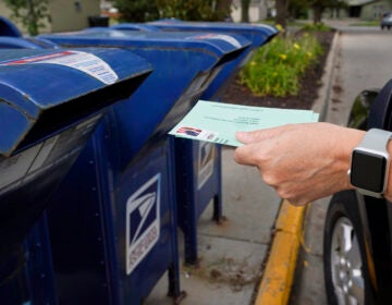 A person drops applications for mail-in-ballots into a mail box