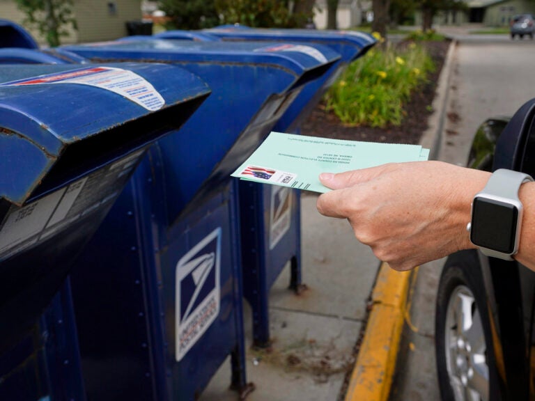 A person drops applications for mail-in-ballots into a mail box