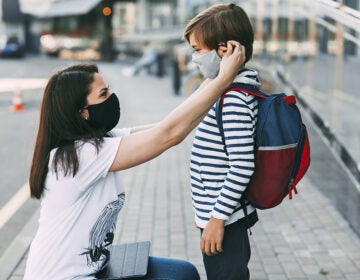 A mother wearing a face mask adjusting a face mask on her son before he goes to school