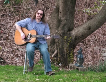 Musician Jay Mage singing and playing guitar outside