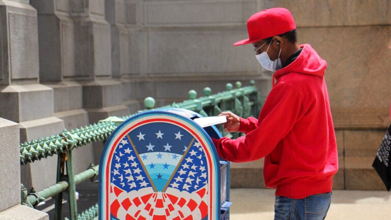 A voter places his mail-in ballot in a box outside City Hall.