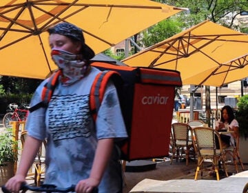 A food delivery courier passes an outdoor dining room in Philly's Rittenhouse neighborhood (Ashta Kunda/Billy Penn)