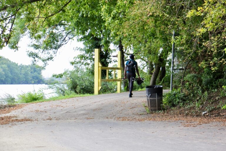A fisherman walks along the Schuylkill River Trail at Bartram's Gardens. (Emma Lee/WHYY)