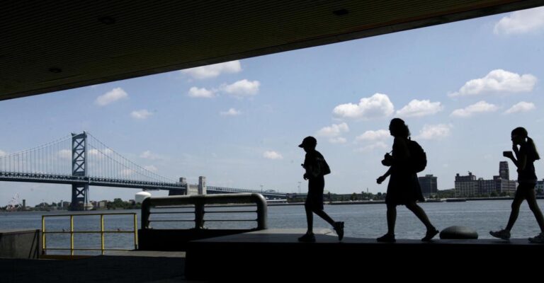 People are silhouetted as they walk on Penn's Landing in view of the Benjamin Franklin Bridge in Philadelphia. (Matt Rourke/AP Photo)