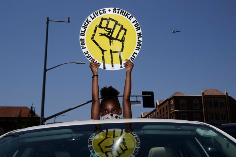 In this July 20, 2020, file photo, Audrey Reed, 8, holds up a sing through the sunroof of a car during a rally in Los Angeles. Ahead of Labor Day, major U.S. labor unions say they are considering work stoppages in support of the Black Lives Matter movement. (AP Photo/Jae C. Hong)
