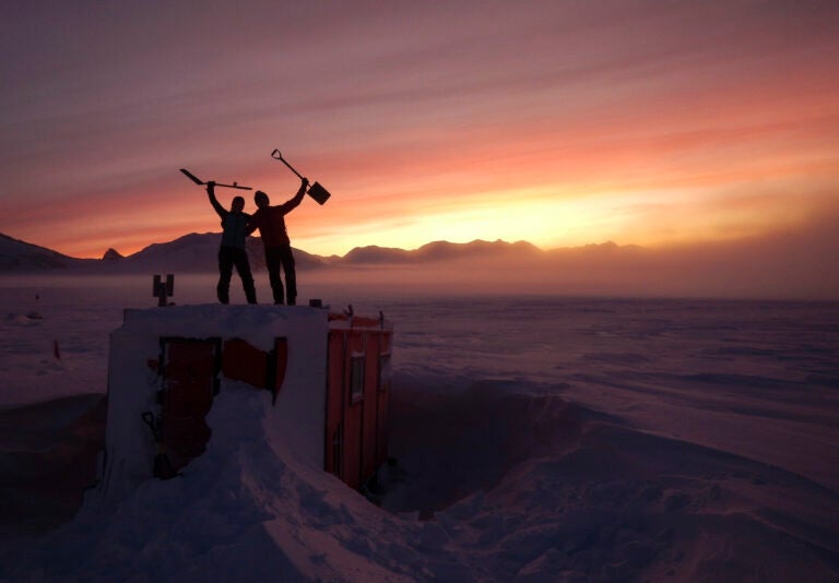 In this handout photo provided by British Antarctic Survey, field guides Sarah Crowsley, left, and Sam Hunt, right, pose for a photo after digging out the caboose, a container used for accommodation that can be moved by a tractor, at Adelaide island, in Antarctica on Friday, June 19, 2020. (Robert Taylor/British Antarctic Survey via AP)