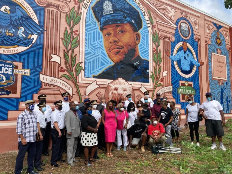 City officials, police officers from the 18th district, and neighborhood residents pose in front of the Sgt. Robert Wilson III mural