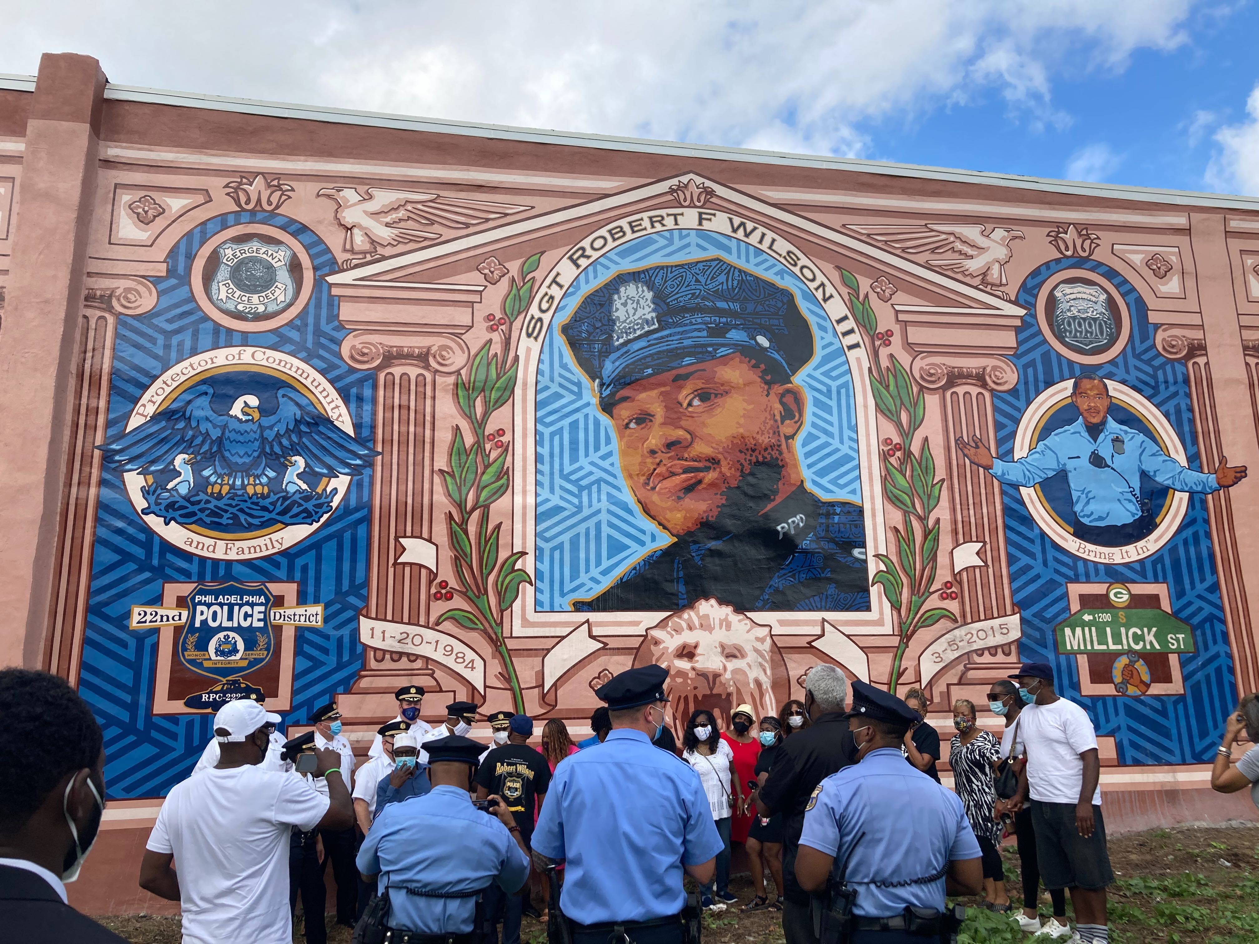 City officials, police officers from the 18th district, and neighborhood residents pose in front of the Sgt. Robert Wilson III mural