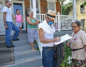 In East Camden, Nelson Berrios signs the petition for nonpartisan elections for Mary Cortes, right on Aug. 22.  (April Saul for WHYY)