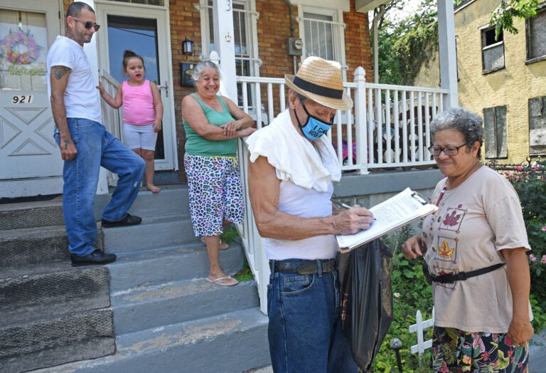 In East Camden, Nelson Berrios signs the petition for nonpartisan elections for Mary Cortes, right on Aug. 22.  (April Saul for WHYY)