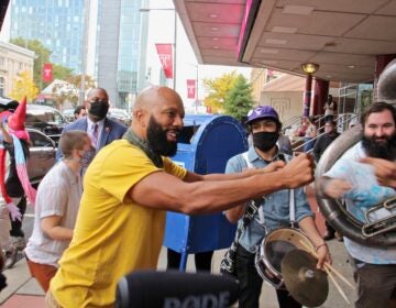 Common, the rapper also known as Lonnie Rashid Lynn, bumps fists with members of the Snack Time Band outside the Liacouras Center after an impromptu jam session. (Emma Lee/WHYY)