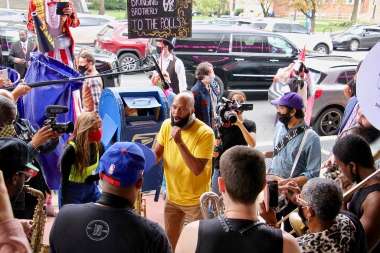 Common jams with the Snacktime Band outside the Liacouras Center, a surprise addition to the Cirque d'Vote entertainment for voters waiting in line there. (Emma Lee/WHYY)