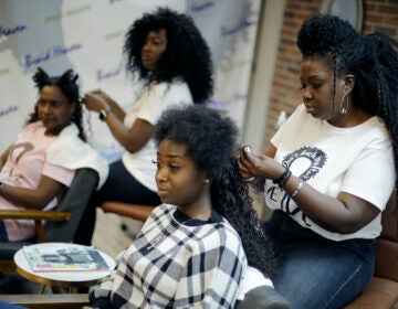 Sisters Shelly Smith, back, and Glynnis Smith, right, braid hair for Bridget Dunmore, left, and Alicia McGee, front at their salon, Braid Heaven, Tuesday, Jan. 28, 2020 in Kansas City, Kan. Legislators are considering whether to revise their states' anti-discrimination laws to ban bias in housing, employment and public accommodations based on hairstyles. (AP Photo/Charlie Riedel)