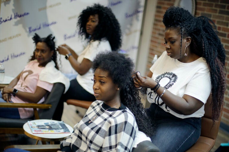 Sisters Shelly Smith, back, and Glynnis Smith, right, braid hair for Bridget Dunmore, left, and Alicia McGee, front at their salon, Braid Heaven, Tuesday, Jan. 28, 2020 in Kansas City, Kan. Legislators are considering whether to revise their states' anti-discrimination laws to ban bias in housing, employment and public accommodations based on hairstyles. (AP Photo/Charlie Riedel)